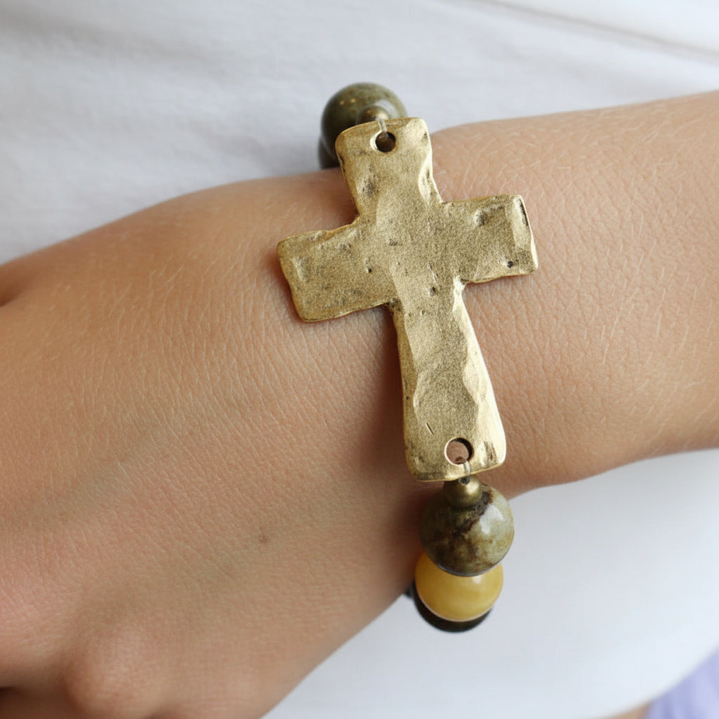Gold cross pendant with beads on a wrist against a white background