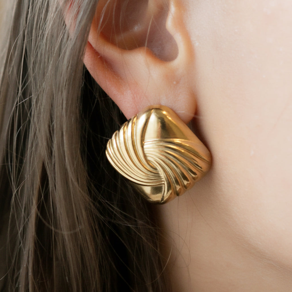 Gold earring worn by a person with dark hair.