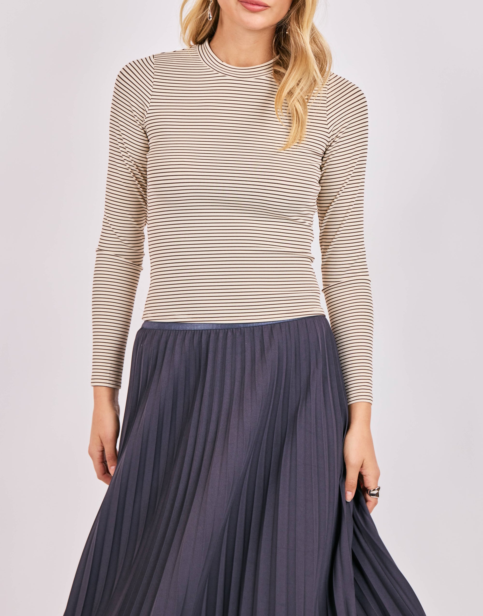 Woman wearing a striped long-sleeve top and pleated skirt on a light gray background