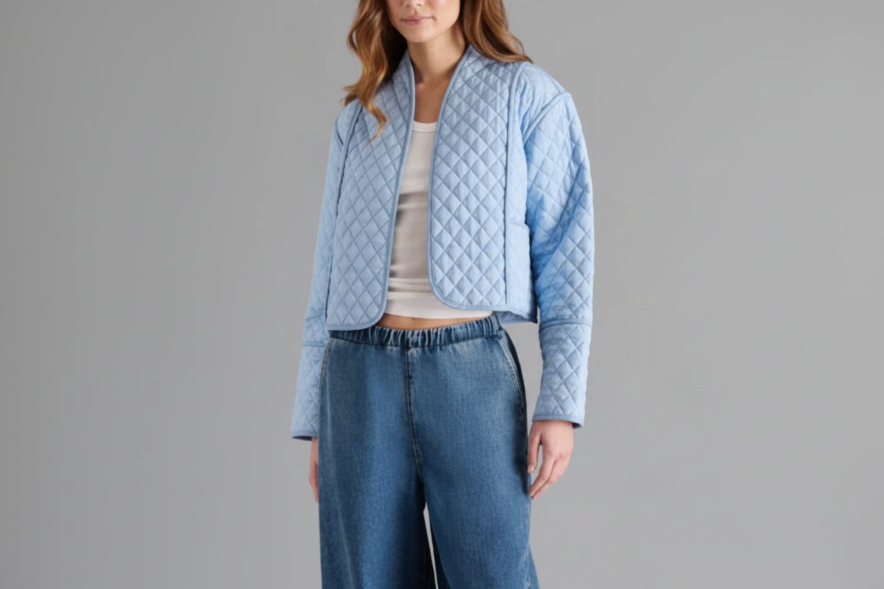 Woman wearing a light blue quilted jacket and blue jeans on a gray background