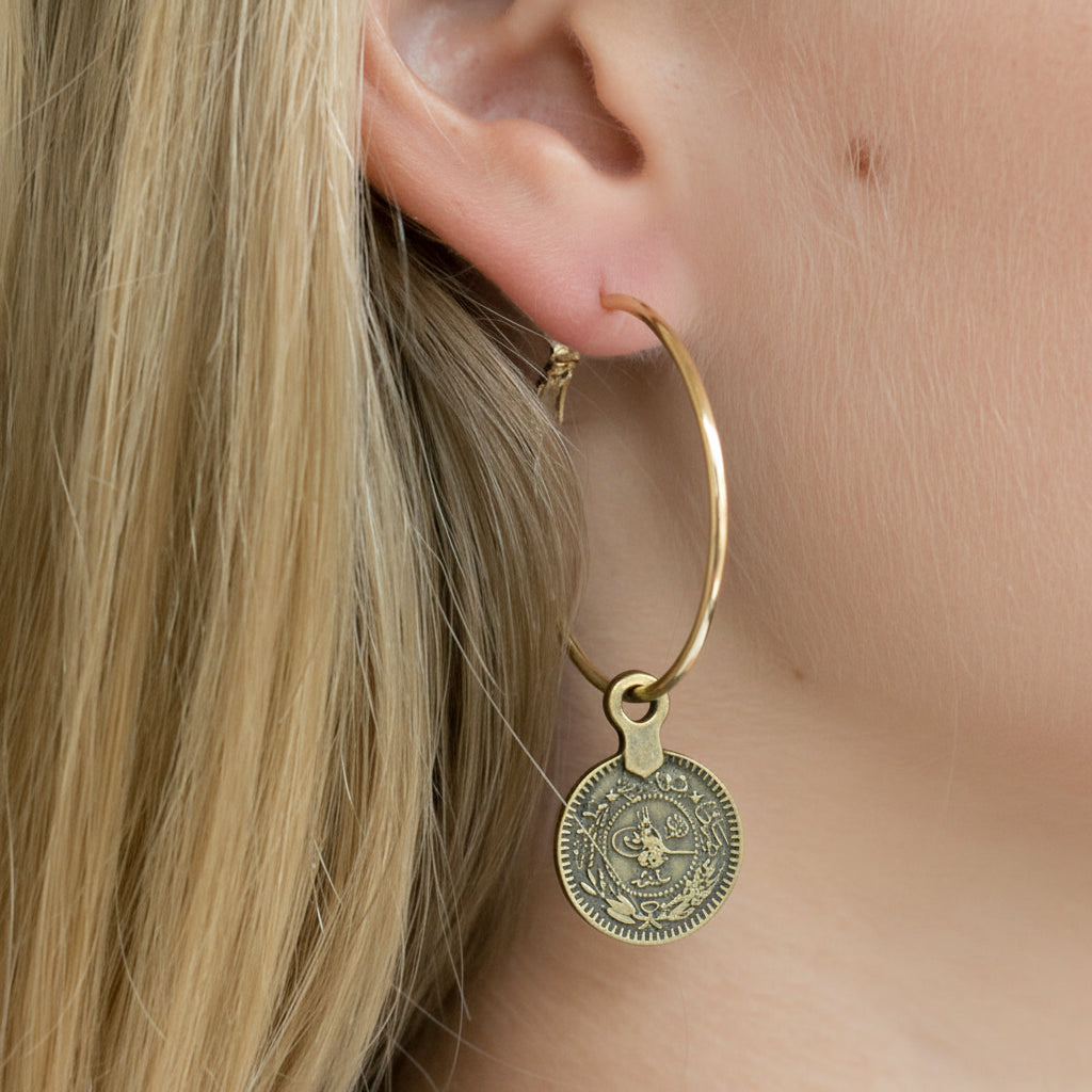 Gold hoop earring with a coin-shaped pendant worn by a person.