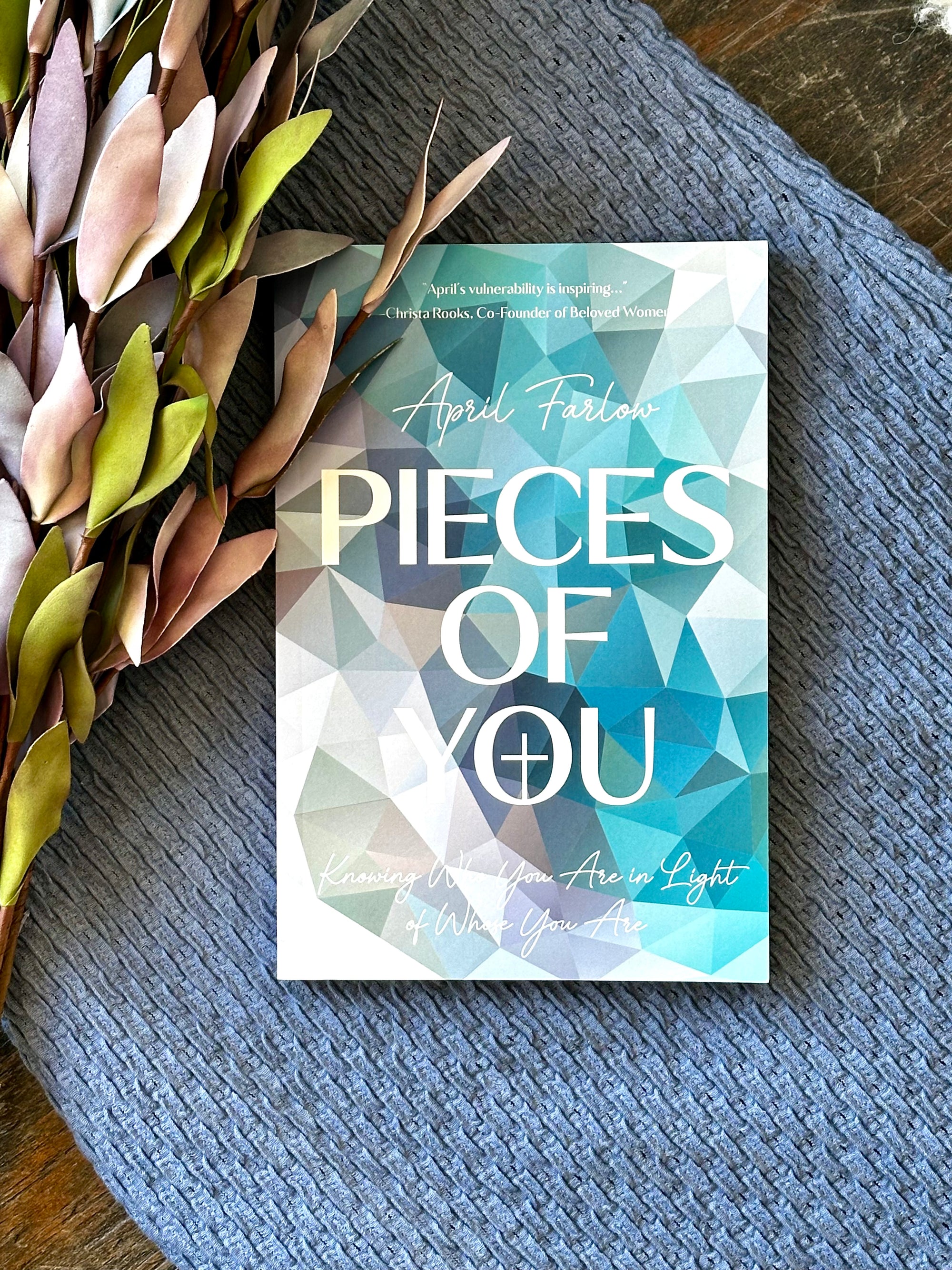 Book titled 'Pieces of You' by April Fialk on a textured surface with decorative leaves.