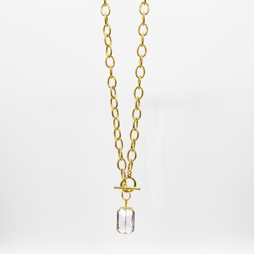 Gold chain with a clear crystal pendant hanging from a white surface.