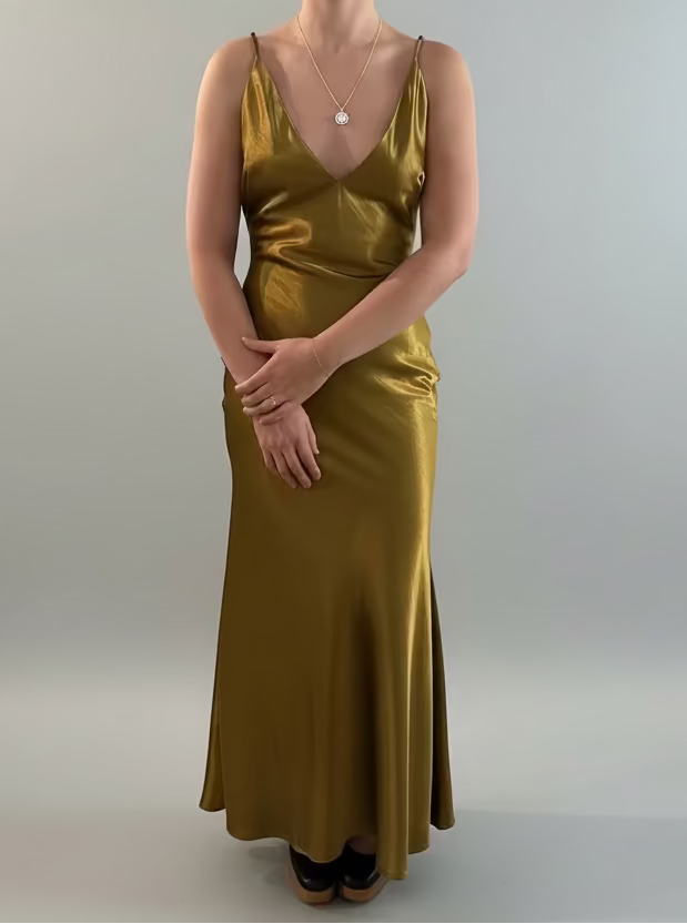 Person wearing a gold satin dress against a plain wall.