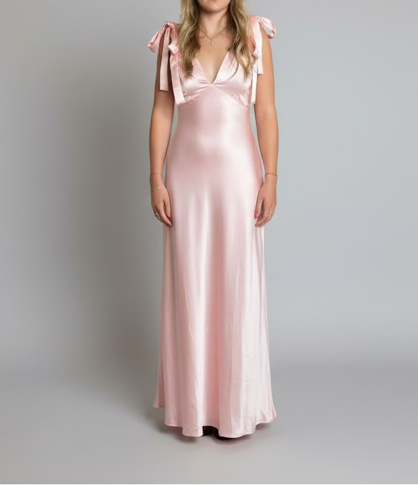 Woman in a pink satin dress standing in a store with various items in the background