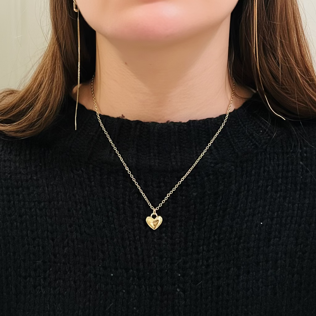 Person wearing a gold necklace with a heart pendant on a black sweater.