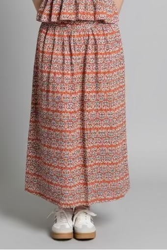 Woman wearing a patterned sleeveless top and long skirt on a gray background