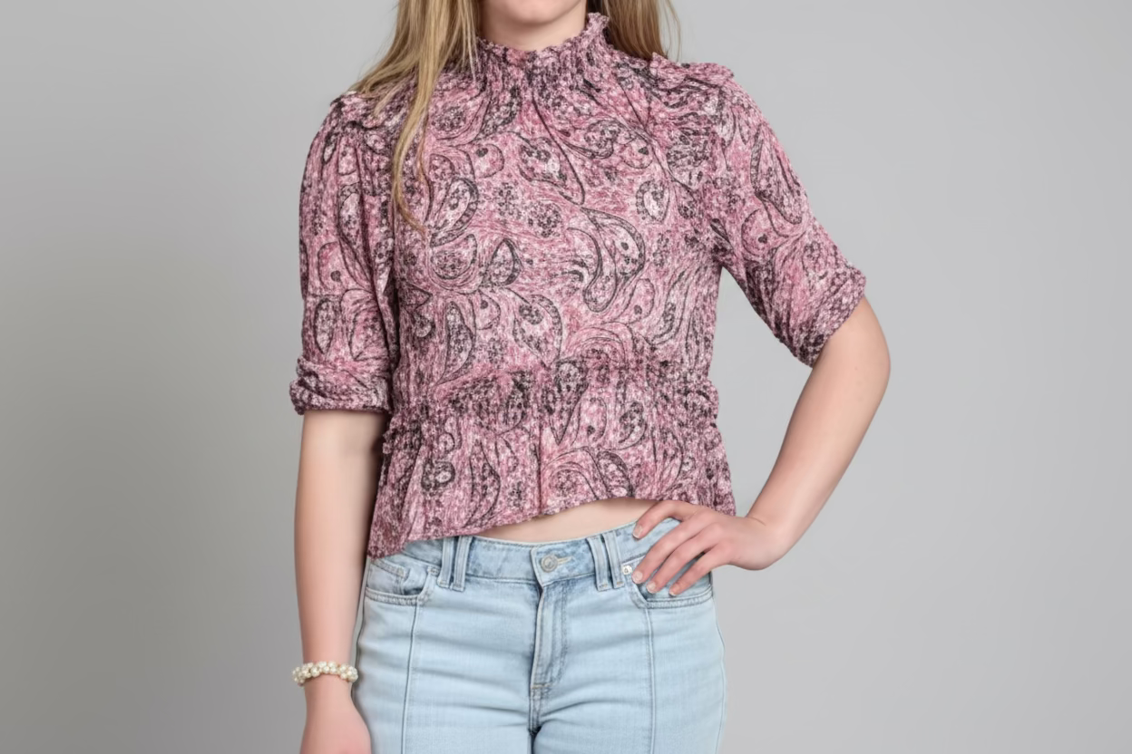 Person wearing a pink patterned blouse and light blue jeans against a gray background