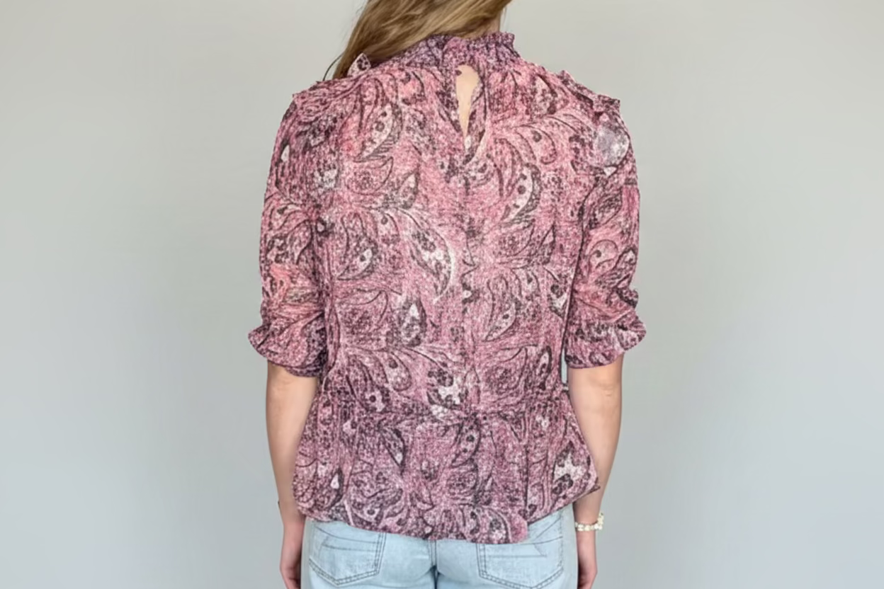 Person wearing a patterned shirt and light blue jeans against a plain background