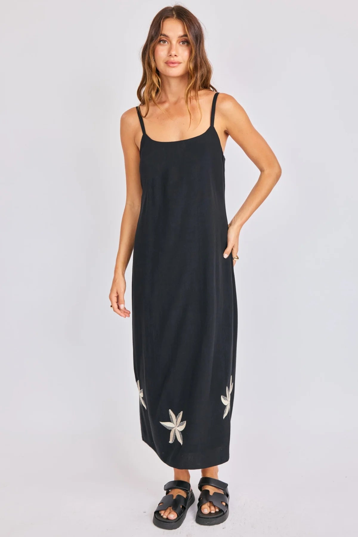 Woman wearing a black slip dress with floral embellishments on a plain background