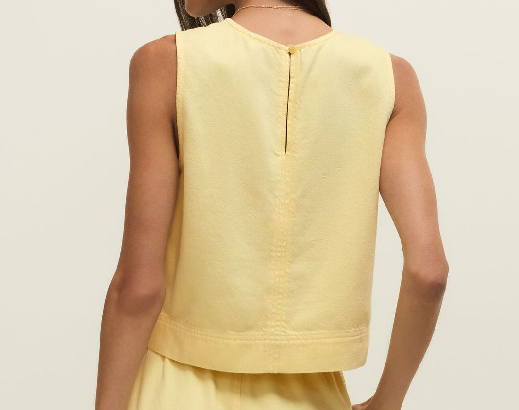 Woman wearing a yellow sleeveless top and pants on a plain background