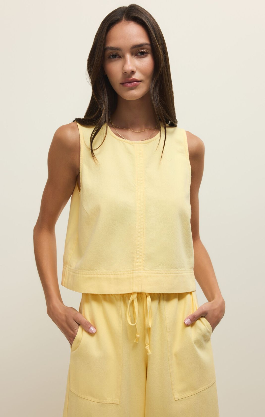 Woman wearing a yellow sleeveless top and pants against a plain background