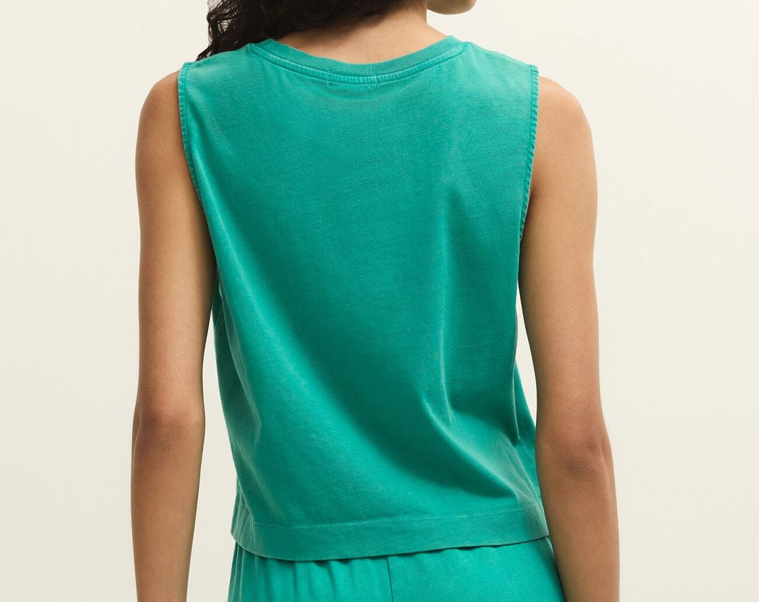 Woman wearing a green sleeveless top and pants against a beige background