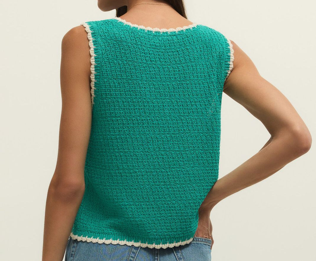 Woman wearing a green sleeveless crochet top with white trim on a beige background