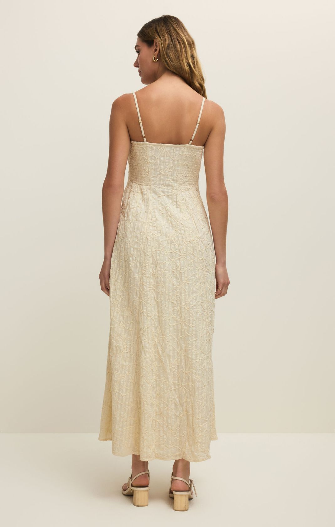 Woman wearing a beige dress with thin straps on a plain background