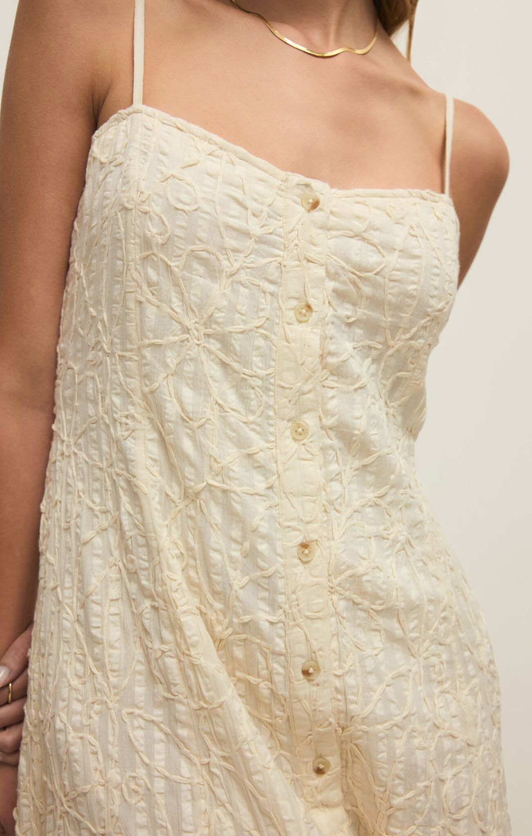 Close-up of a cream-colored dress with button details on a plain background