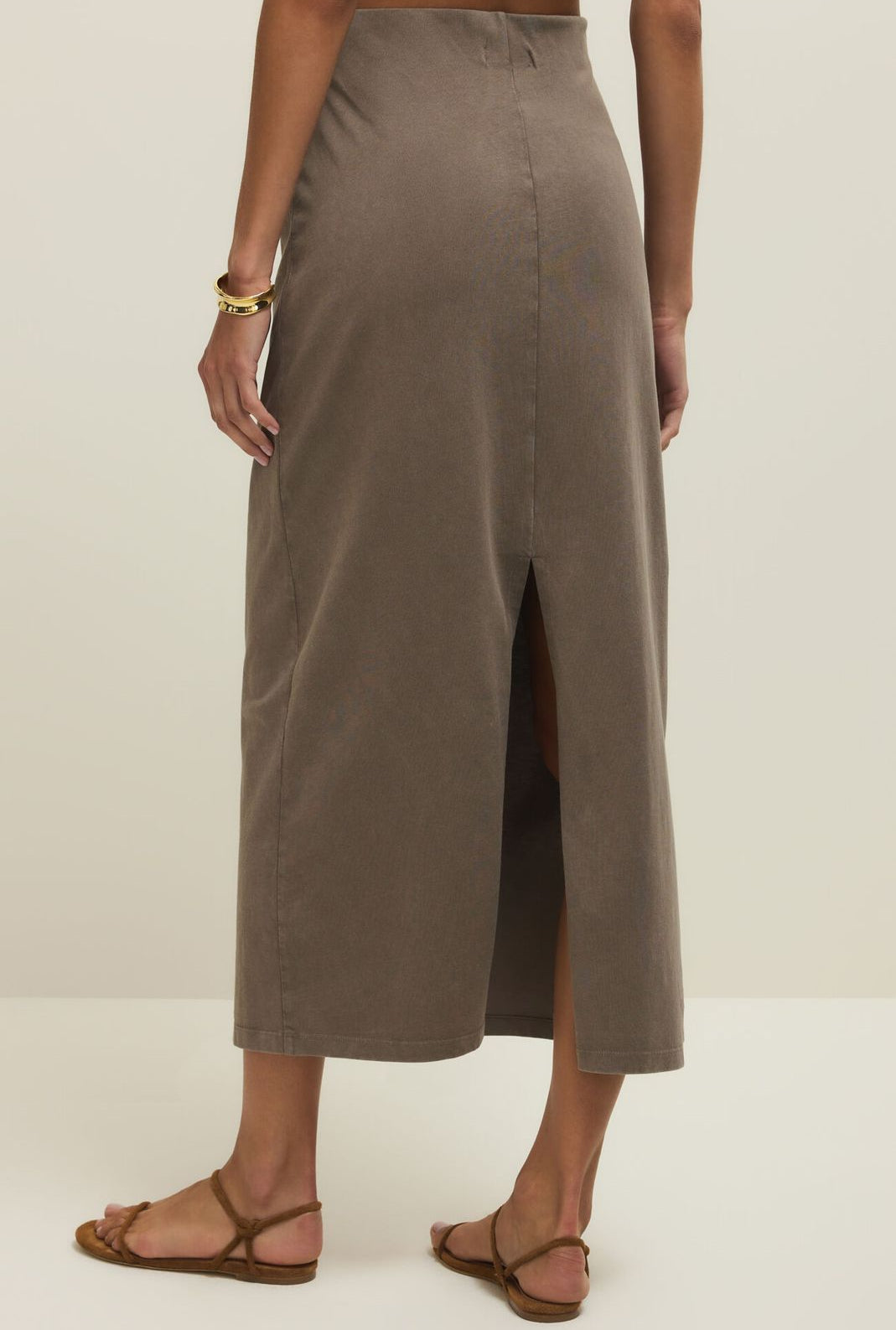 Person wearing a long, light brown skirt on a plain background