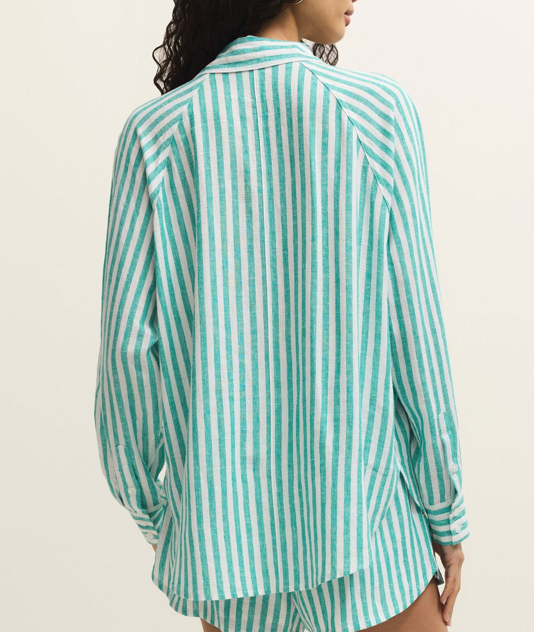 Woman wearing a green and white striped shirt and shorts on a beige background