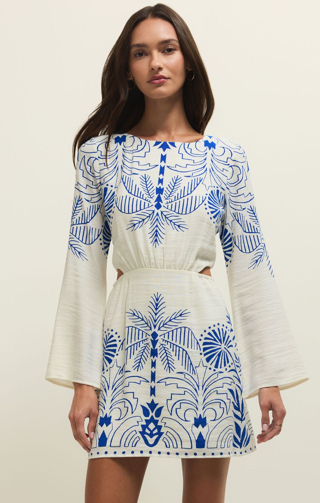 Woman wearing a white dress with blue geometric patterns on a plain background
