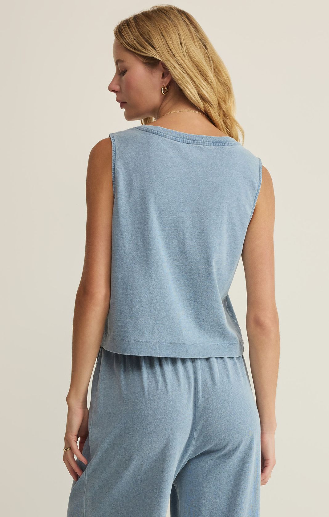 Woman wearing a light blue sleeveless top and pants on a beige background