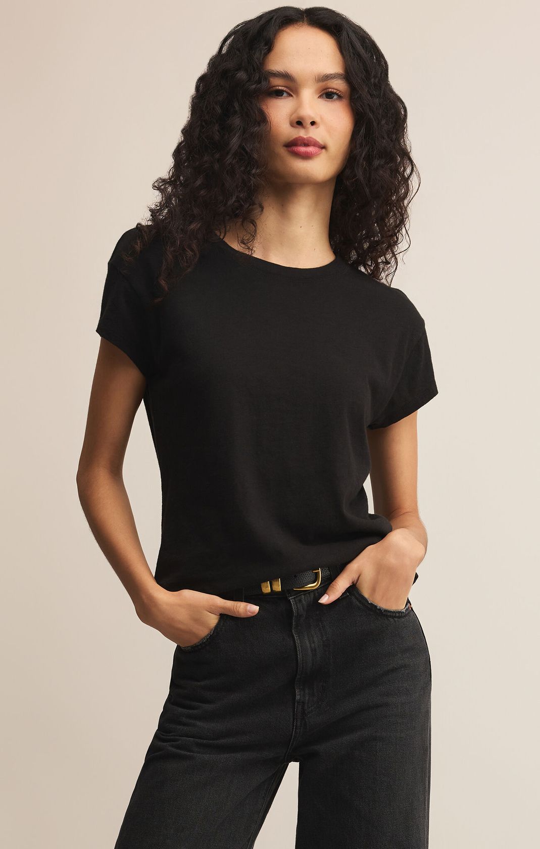 Woman wearing a black t-shirt and black pants against a beige background