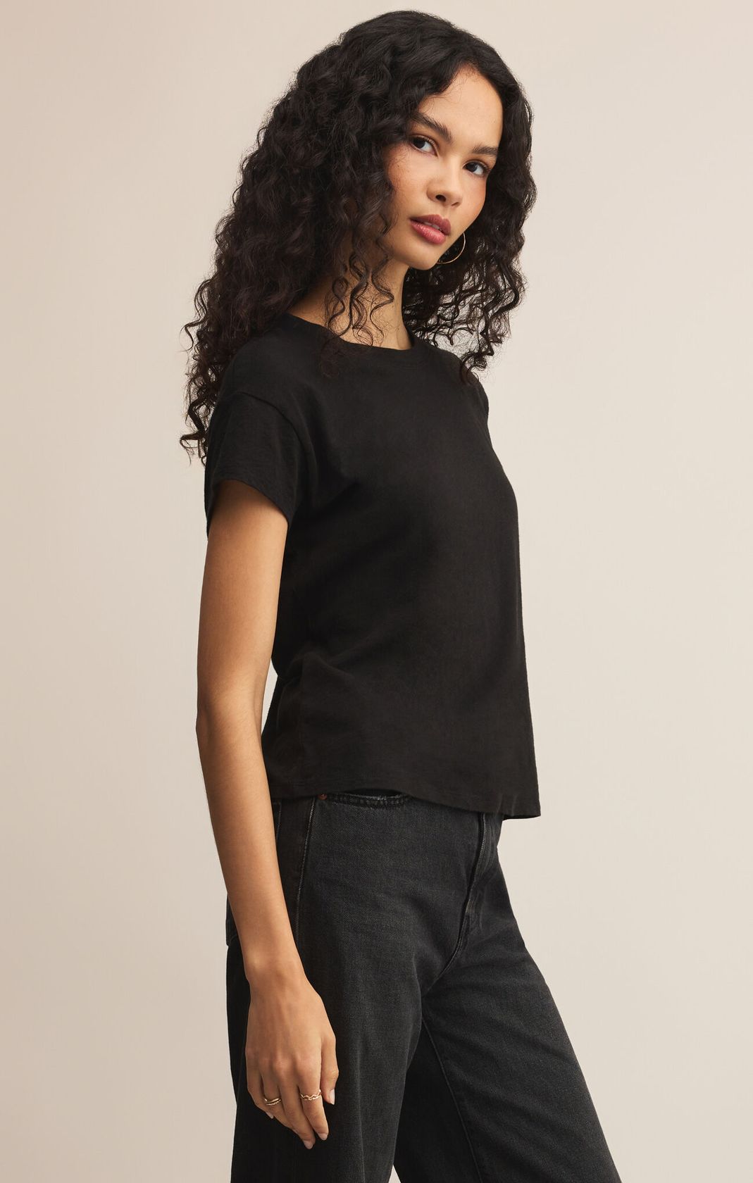Woman wearing a black t-shirt and black pants against a beige background