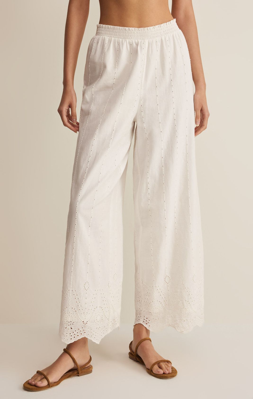Person wearing white lace pants on a beige background. European Summer. Embroidered pants