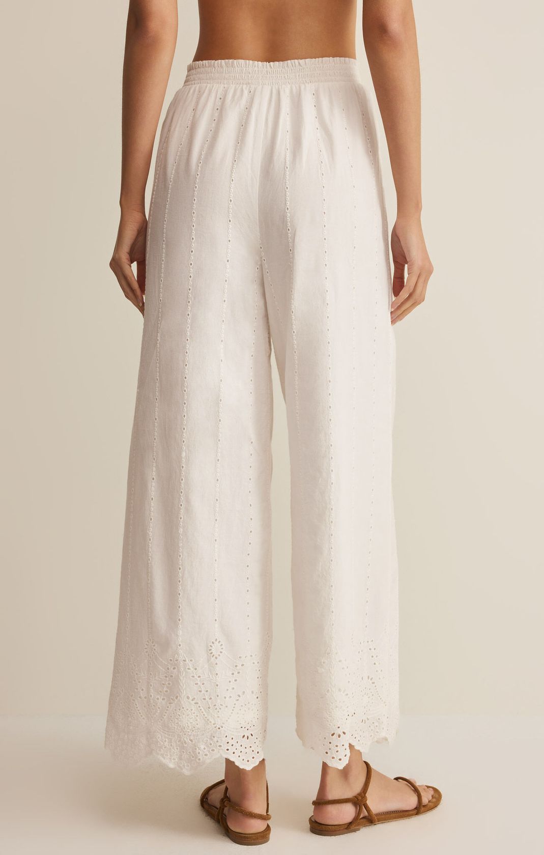 Person wearing white lace pants on a beige background. European Summer. Embroidered pants