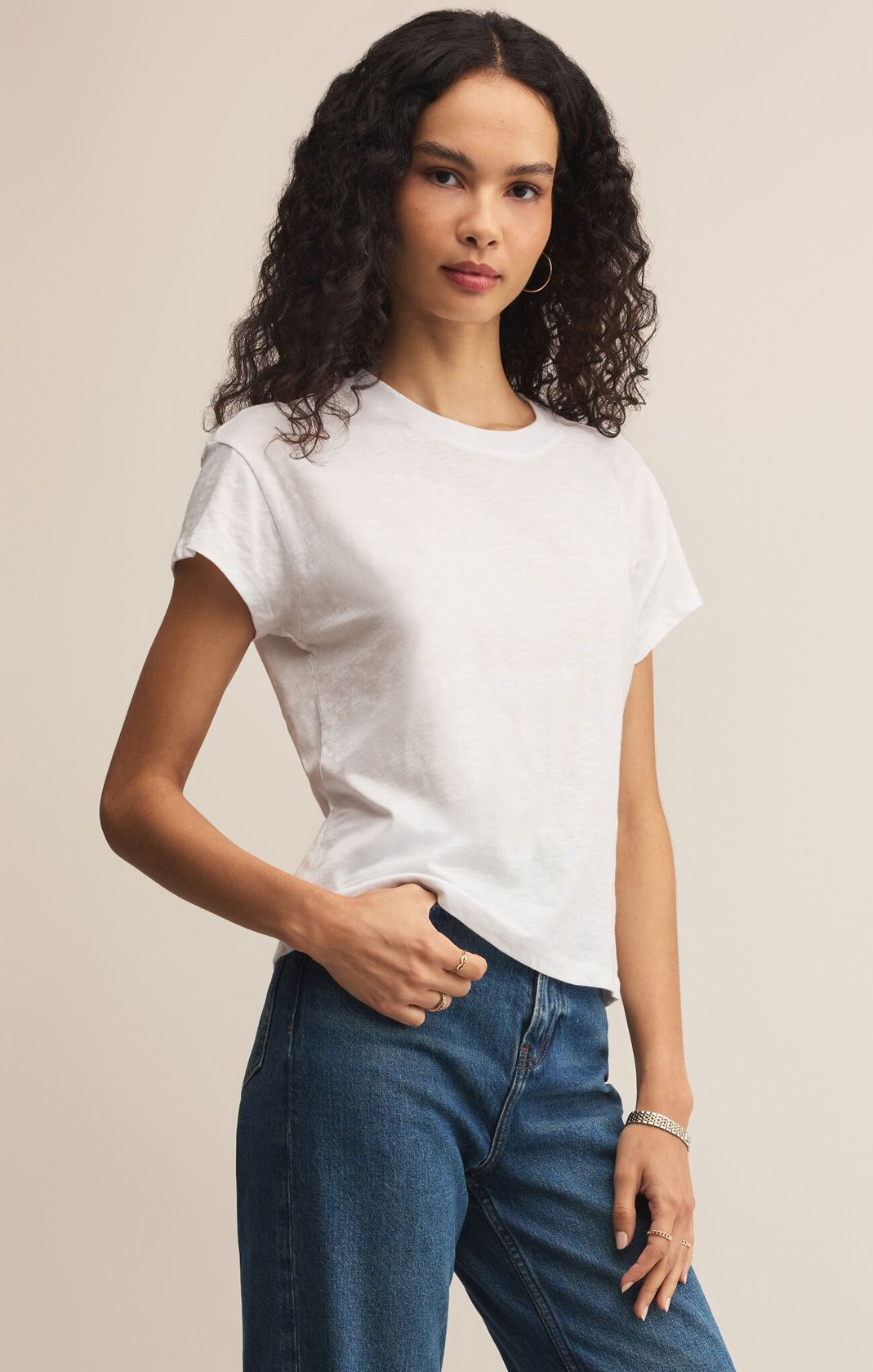 Woman wearing a white t-shirt and blue jeans against a beige background