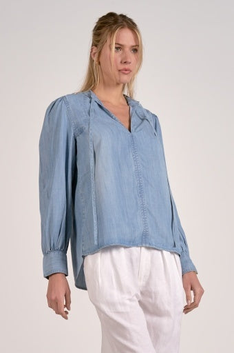 Woman wearing a light blue denim blouse and white pants on a plain background