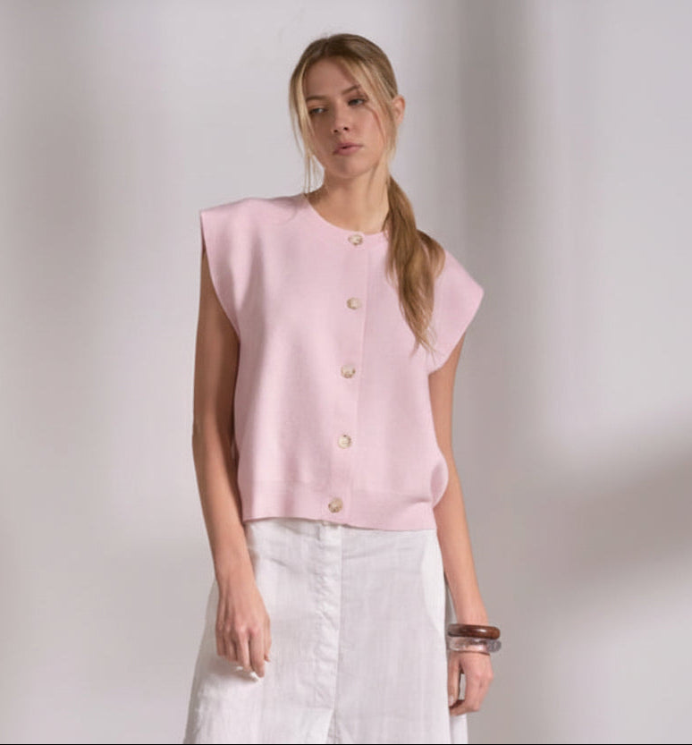 Woman wearing a light pink sleeveless blouse with buttons on a plain background