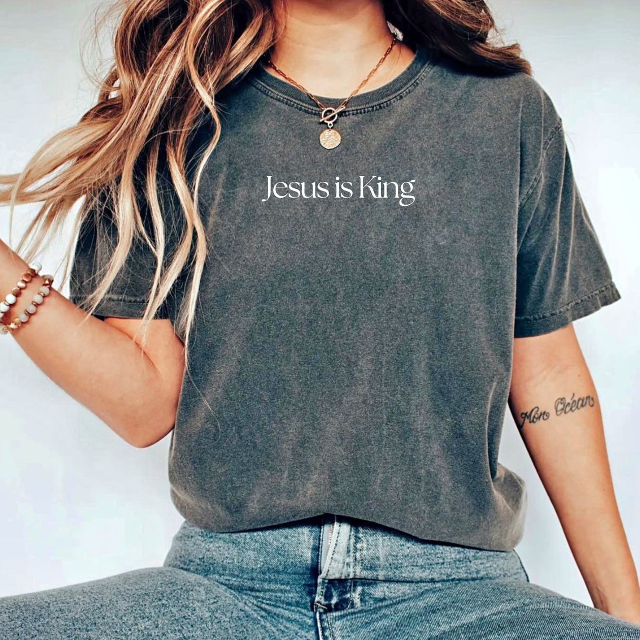 Person wearing a t-shirt with 'Jesus is King' text on a plain background