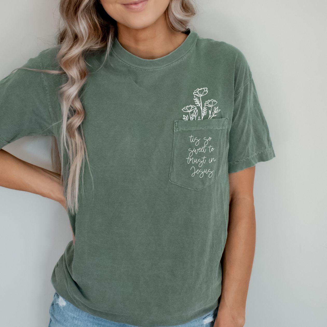 Person wearing a green t-shirt with floral design and text "tis so sweet to trust in Jesus"