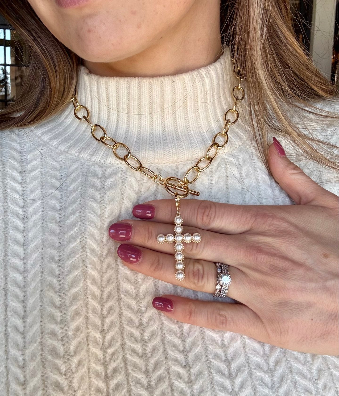 Close-up of a person wearing a gold chain necklace with a cross pendant, holding it with their hand.