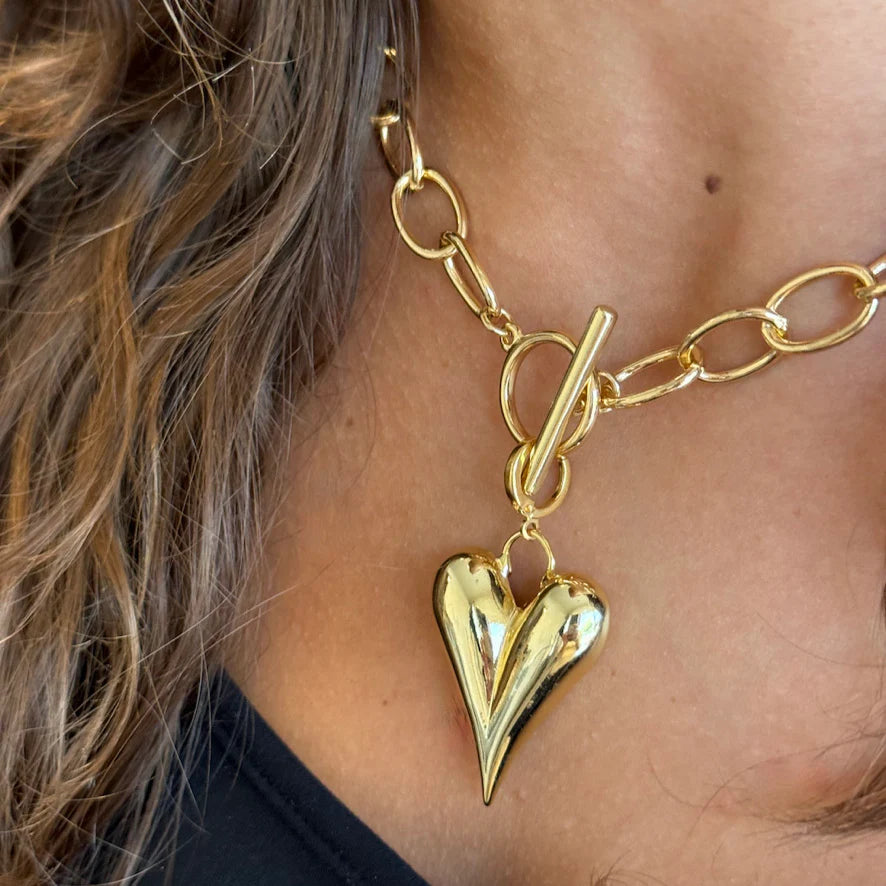 Gold chain necklace with a heart pendant worn by a person