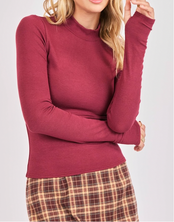 Person wearing a maroon long-sleeve top and plaid pants on a plain background