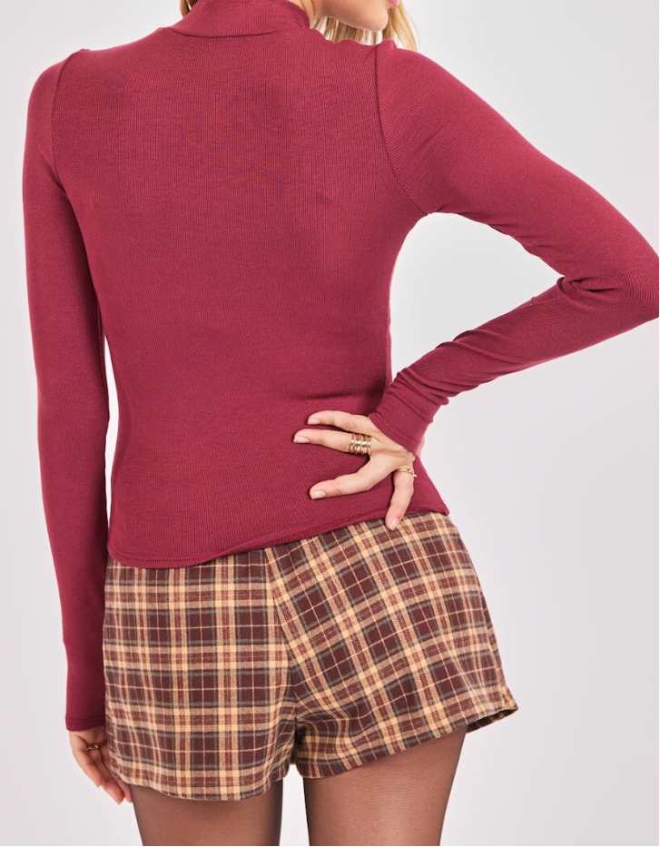 Person wearing a maroon long-sleeve top and plaid shorts on a white background