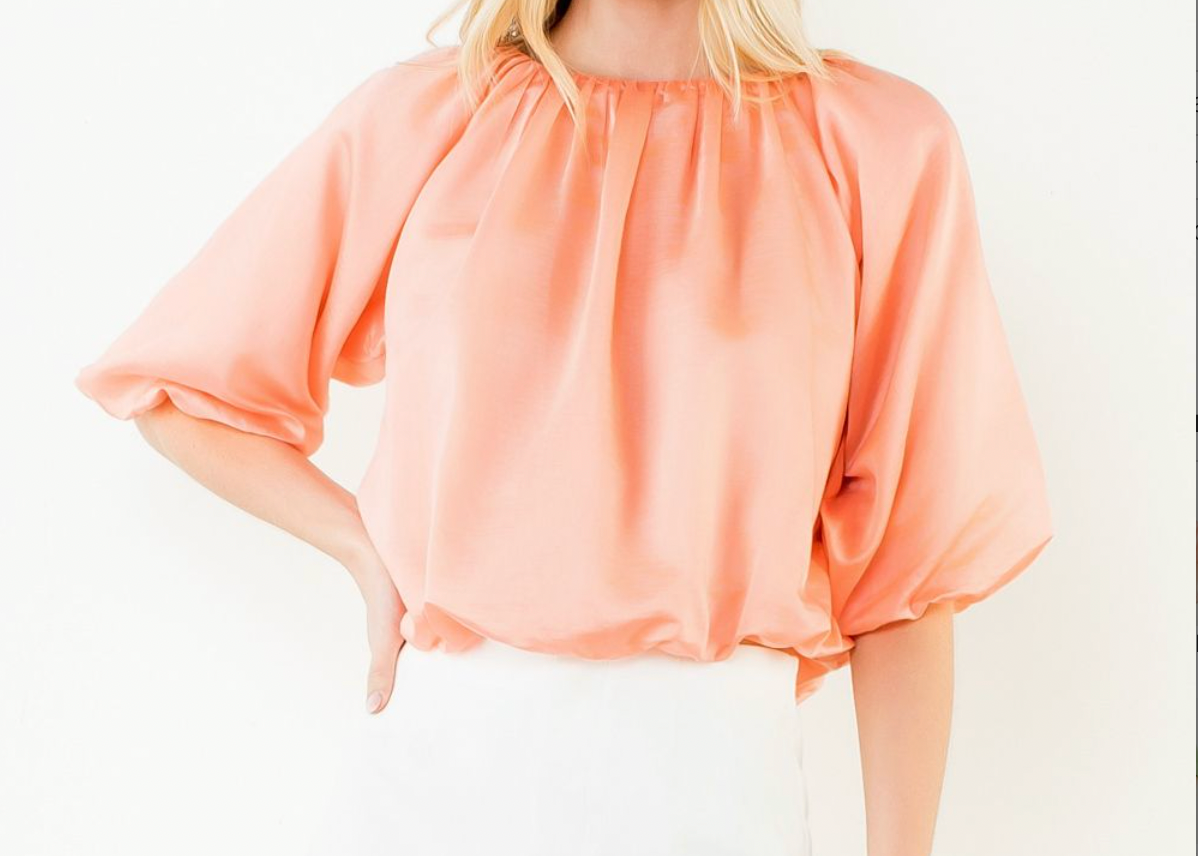 Woman wearing a peach blouse with balloon sleeves on a white background