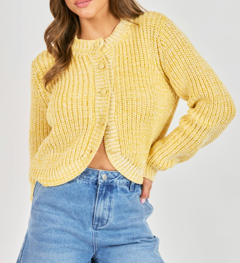 Person wearing a yellow knitted cardigan and blue jeans on a plain background