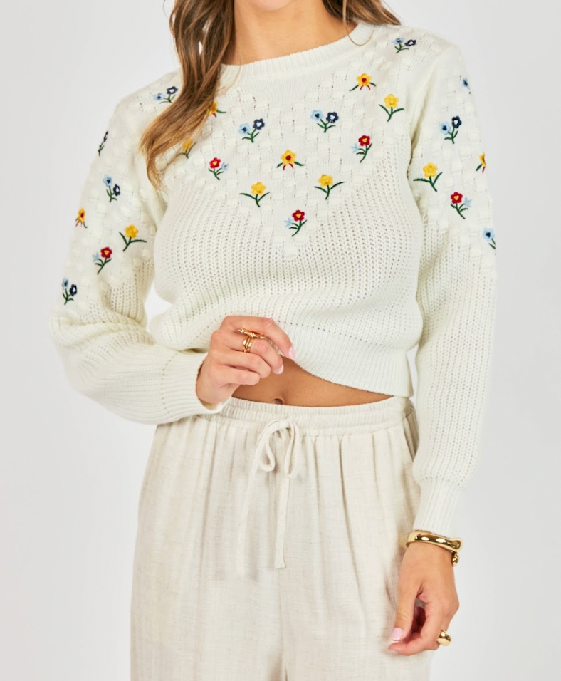White sweater with floral embroidery worn by a person on a white background
