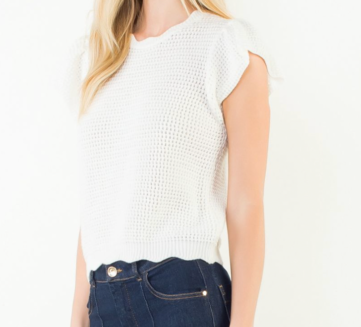 Person wearing a white sleeveless top and dark jeans on a plain background