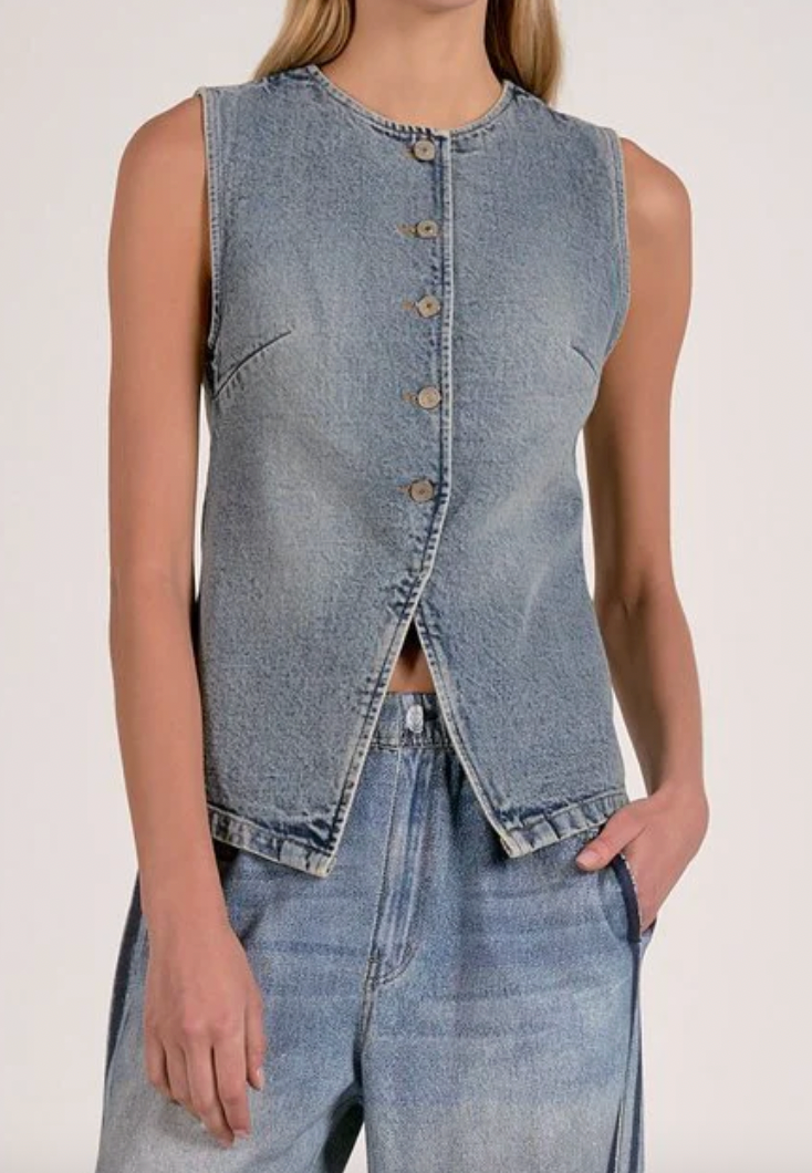 Person wearing a sleeveless denim vest and jeans on a plain background