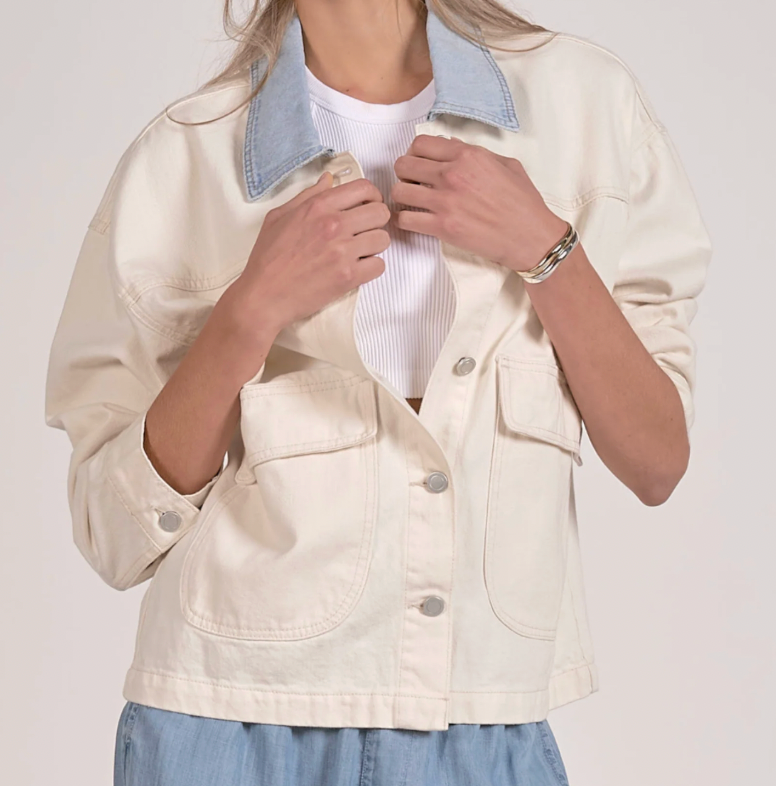 Person wearing a cream-colored denim jacket with a white shirt underneath on a plain background