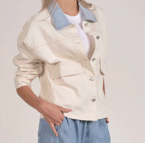 Person wearing a beige jacket with denim collar and blue jeans on a plain background
