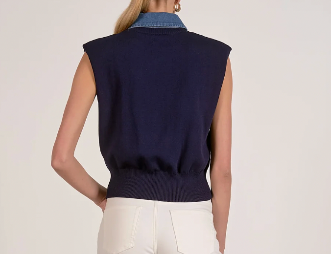 Person wearing a navy blue sleeveless sweater over a denim shirt on a light background