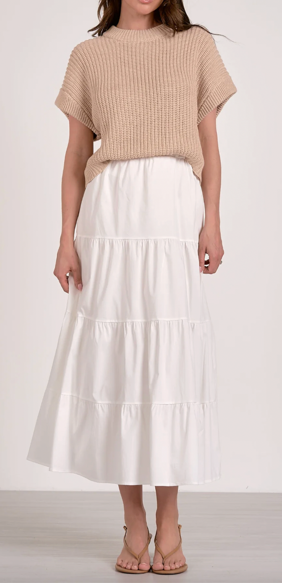 Woman wearing a beige top and white tiered skirt on a plain background
