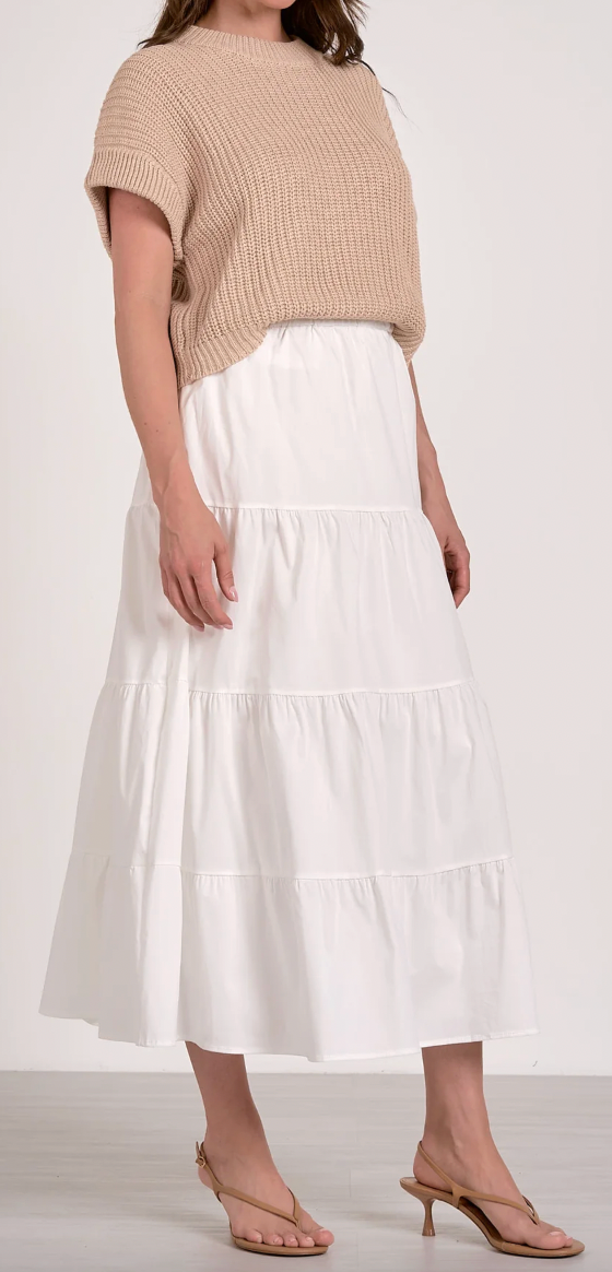 Woman wearing a beige sweater and white tiered skirt on a plain background