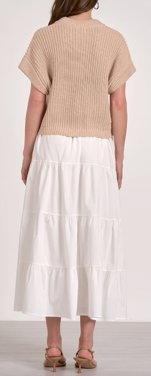 Woman wearing a beige top and white tiered skirt on a plain background