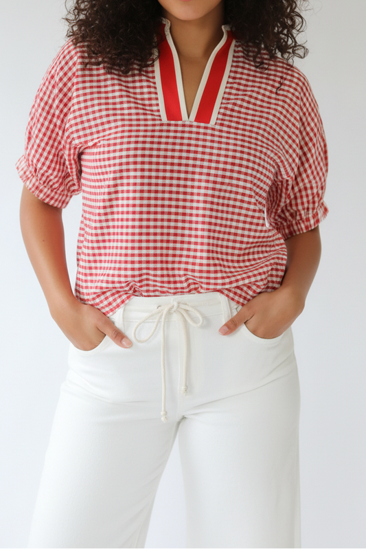 Person wearing a red and white checkered blouse with white pants on a plain background