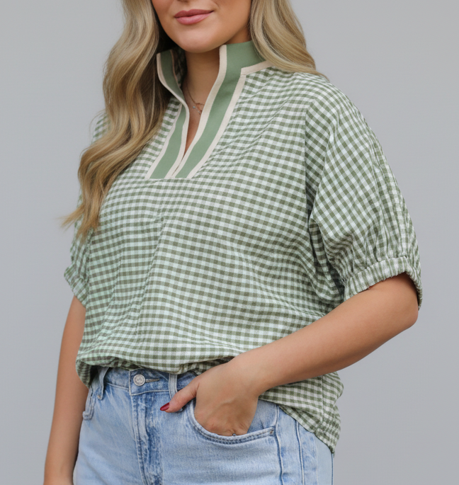 Woman wearing a green checkered shirt and light blue jeans with a blurred background